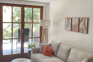Een woonkamer met een bank, een lamp en uitzicht op een balkon met planten en een hek.