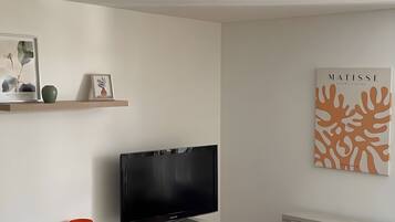 Un salon doté d’un téléviseur à écran plat, d’une estampe botanique encadrée et d’une œuvre d’art abstraite accrochée au mur.