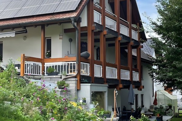 Un immeuble à plusieurs étages doté de balcons, un jardin agrémenté de fleurs et un vélo.