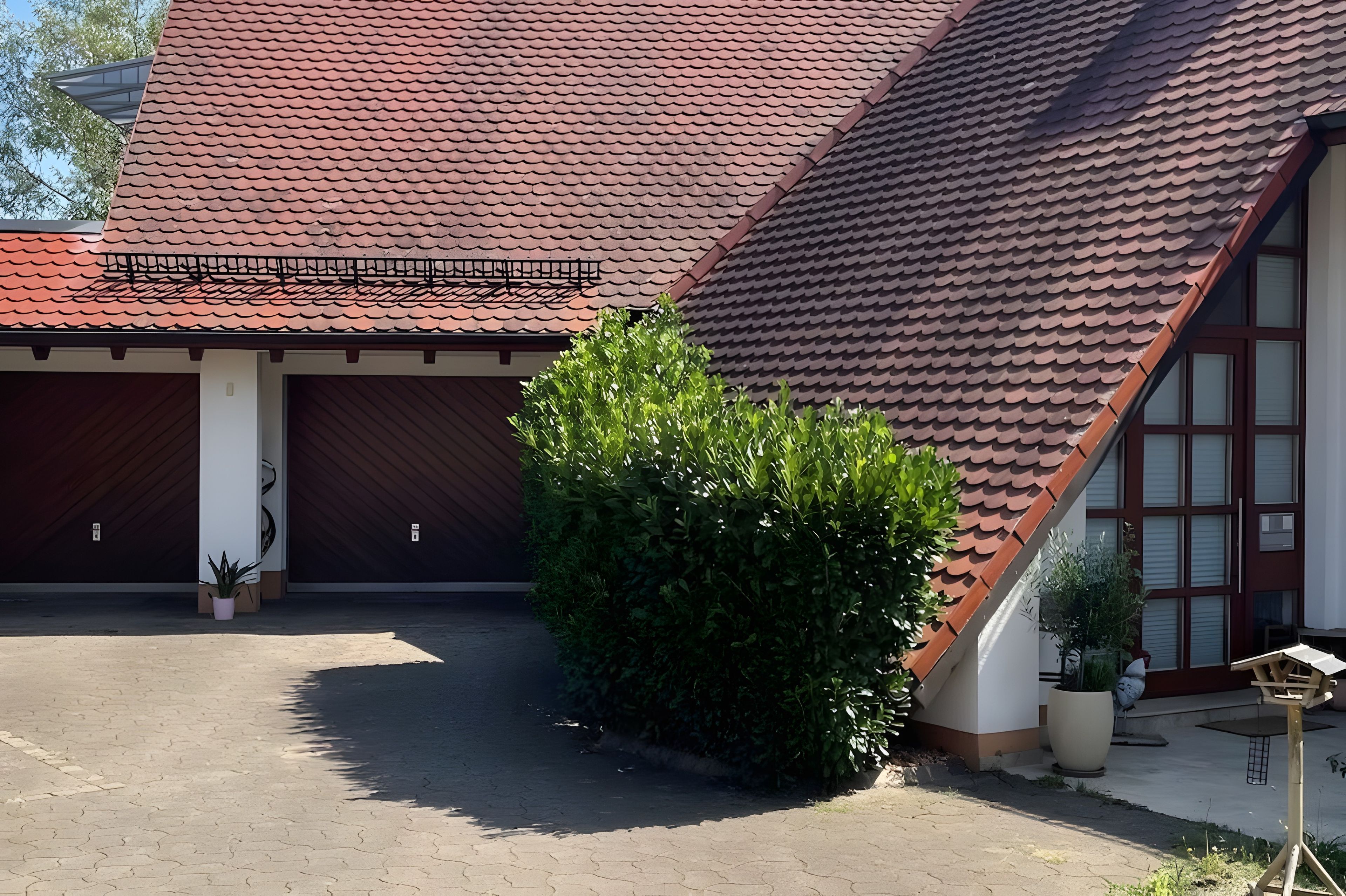 Ein Gebäude mit geneigtem Dach, einer überdachten Auffahrt und einem kleinen Garten mit Kübelpflanzen.