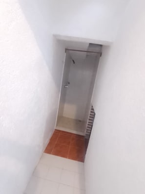 A narrow hallway with a shower area at the end, featuring a tiled floor and white walls.