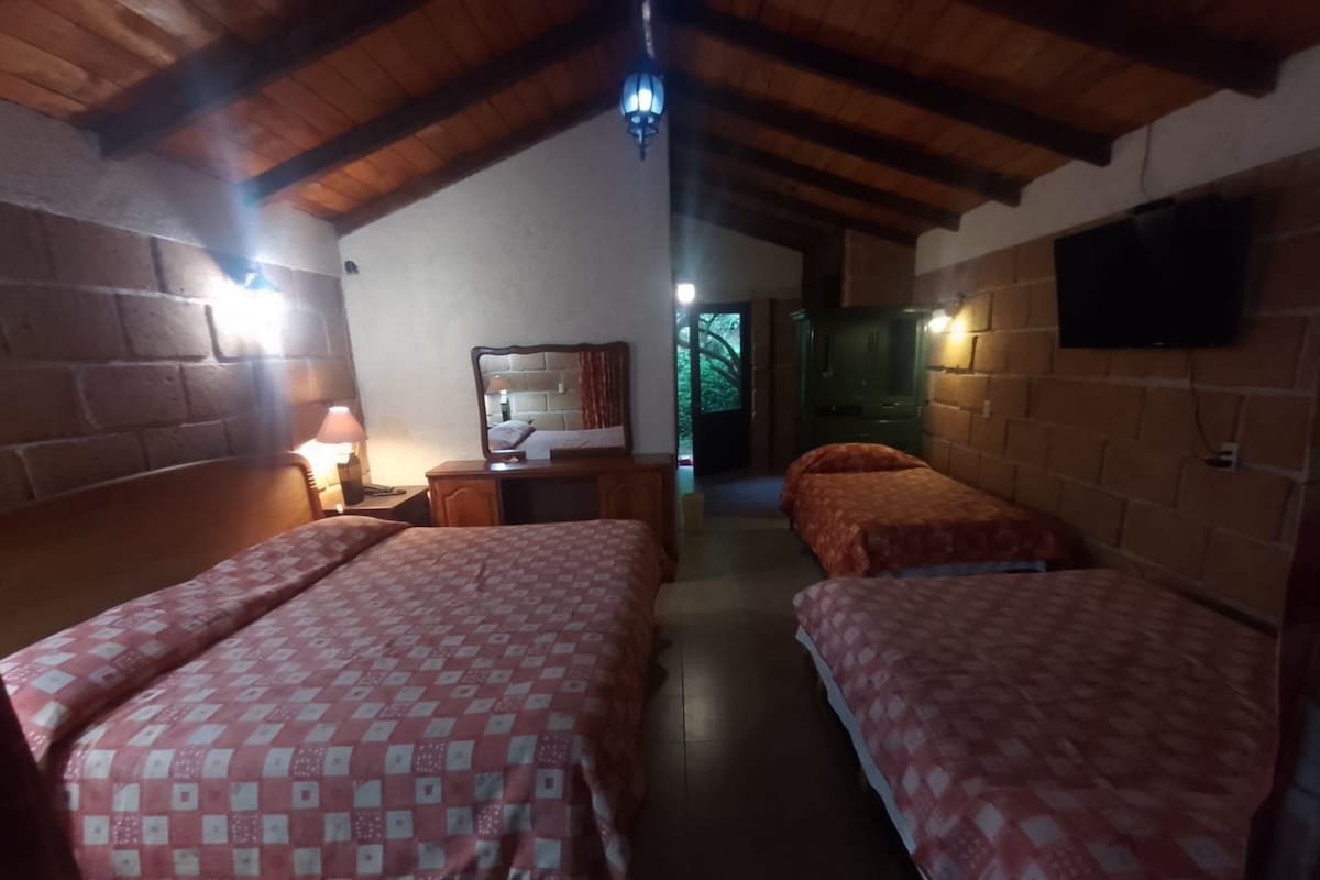 A room with two beds, a wooden ceiling, a brick wall, a television, and a window.