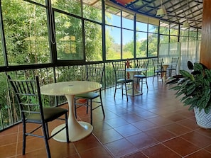 An indoor space with a glass wall, a round table, chairs, and potted plants.