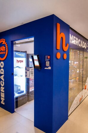 Een blauwe gevel met een digitale kiosk, een vriezer met 'hope' branding en een 'Mercado' bord.
