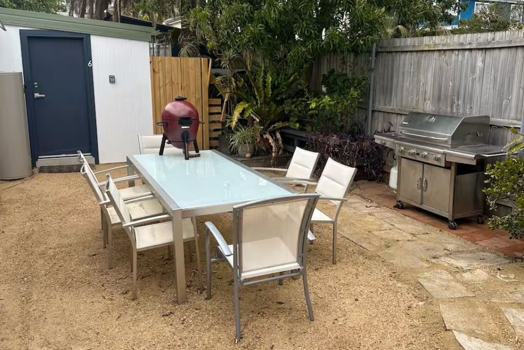 A backyard with a glass-top table and chairs, a barbecue grill, and a shed.