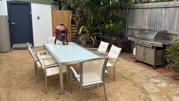 A backyard with a glass-top table and chairs, a barbecue grill, and a shed.