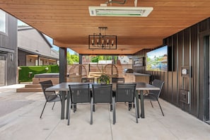 Une terrasse extérieure avec une table et des chaises, un luminaire suspendu et une vue sur un paysage montagneux.