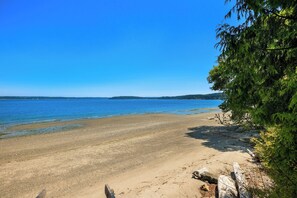 Ein Strand mit klarem, blauem Wasser, einem sandigen Ufer und einer bewaldeten Gegend.