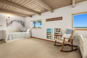 Ein gemütliches Zimmer mit einem Bett, einem Schaukelstuhl, einem Bücherregal und einem Schild mit der Aufschrift 'BEACH HOUSE'.