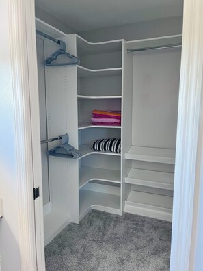 Ein begehbarer Kleiderschrank mit offenen Regalen, einer Kleiderstange und einem Stauraum für zusammengefaltete Kleidung.