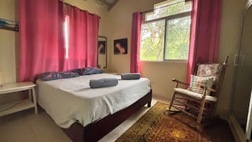 A bedroom with a bed, a chair, a window, and a rug.