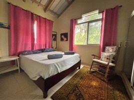 Un dormitorio con cama, una silla, un ventanal y una alfombra.