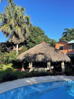 A thatched-roof structure with a pool in the foreground. - Casa Baldoria Tropical Escape (Cabrera)