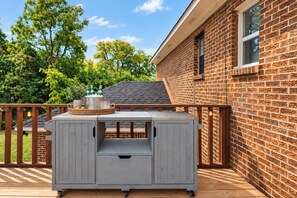 Un barbecue avec un panier de fruits et des bouteilles, le tout posé sur une terrasse en bois.