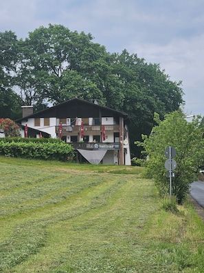 Un edificio de dos pisos con un balcón, rodeado de vegetación.