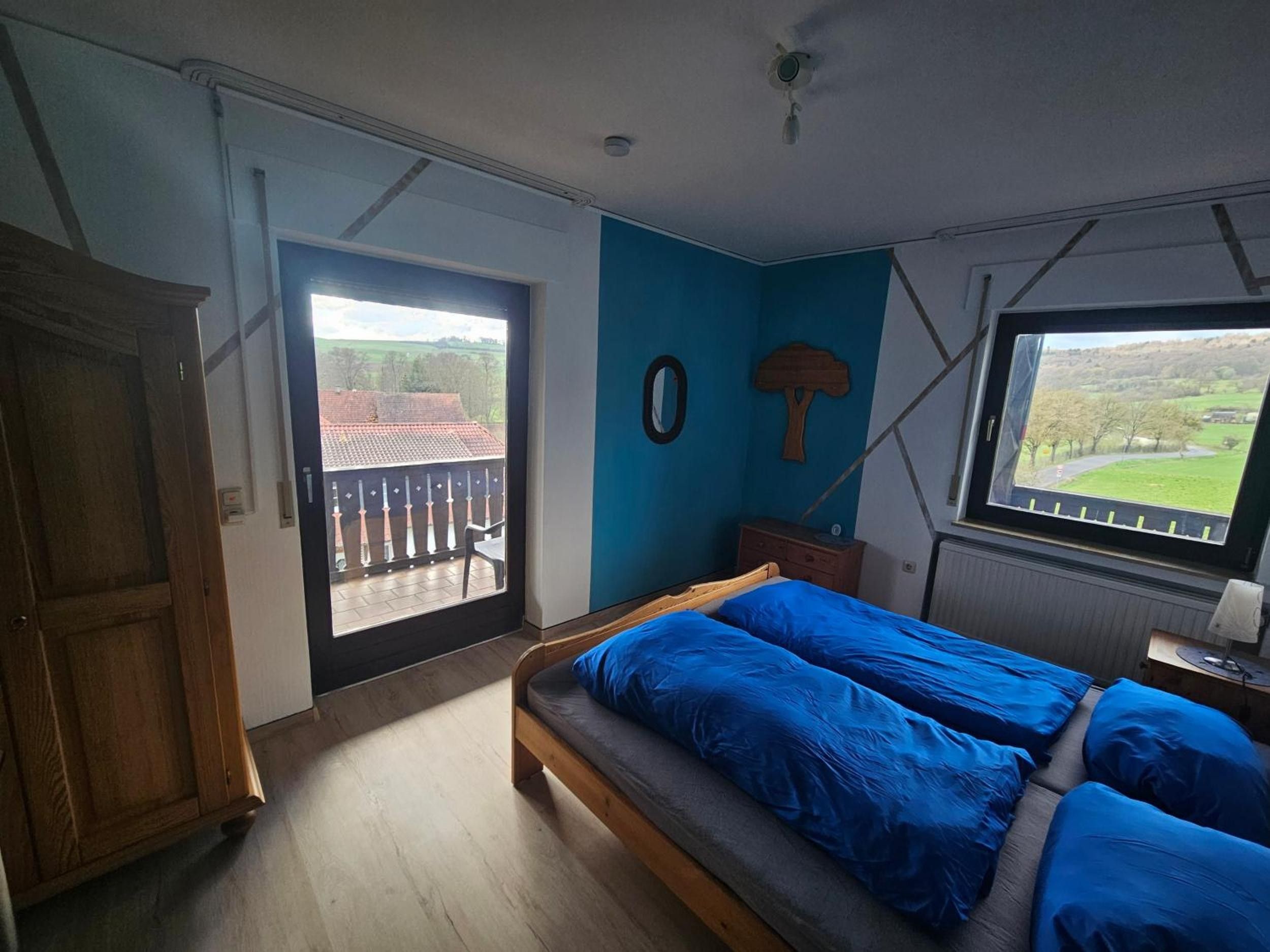 A bedroom with a bed, a window with a view, a door, and a wooden wardrobe.