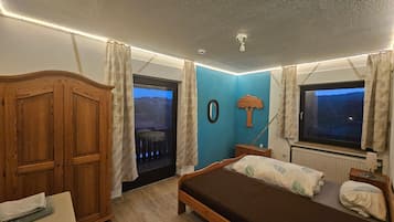 Un dormitorio con cama, un armario de madera, cómoda, ventana con cortinas y vista al exterior.