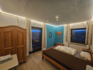 Un dormitorio con cama, un armario de madera, cómoda, ventana con cortinas y vista al exterior.