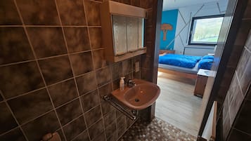 Un baño con lavamanos, espejo y vista a un dormitorio con cama y ventana.