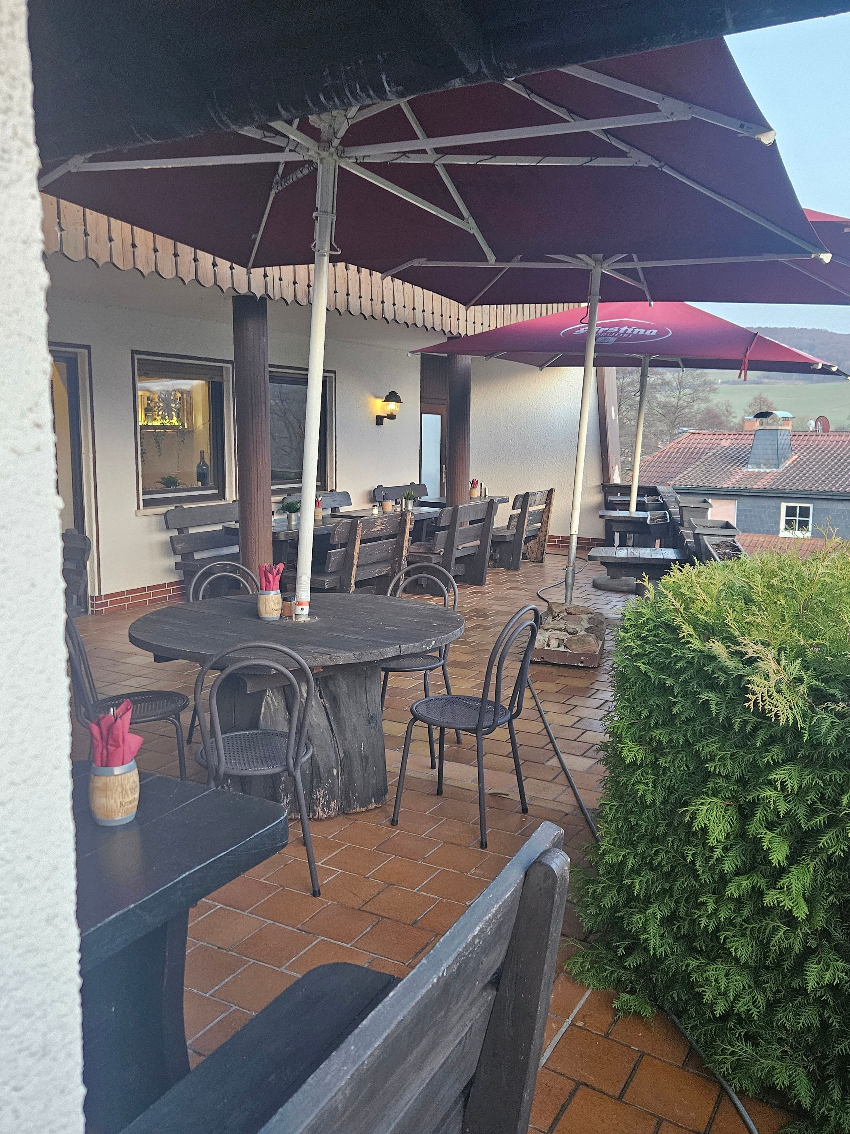 Un patio exterior con mesas y sillas, una parrilla de barbacoa y un gran parasol que da sombra.