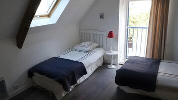 A bedroom with a skylight, a bed with a white headboard, a bedside table with a red lamp, and a window with curtains.
