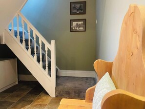 A staircase with white balusters leading to a landing, a wooden chair with a cushion, and two framed pictures on the wall. - Stylish Stamford Apartment with Rooftop Terrace (Lincolnshire)