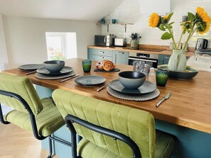 A modern kitchen with a wooden countertop, a dining table set with plates, bowls, and a vase with flowers. - Stylish Stamford Apartment with Rooftop Terrace (Lincolnshire)