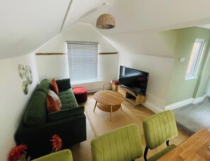 A cozy living room with a green sofa, a wooden coffee table, and a television. - Stylish Stamford Apartment with Rooftop Terrace (Lincolnshire)