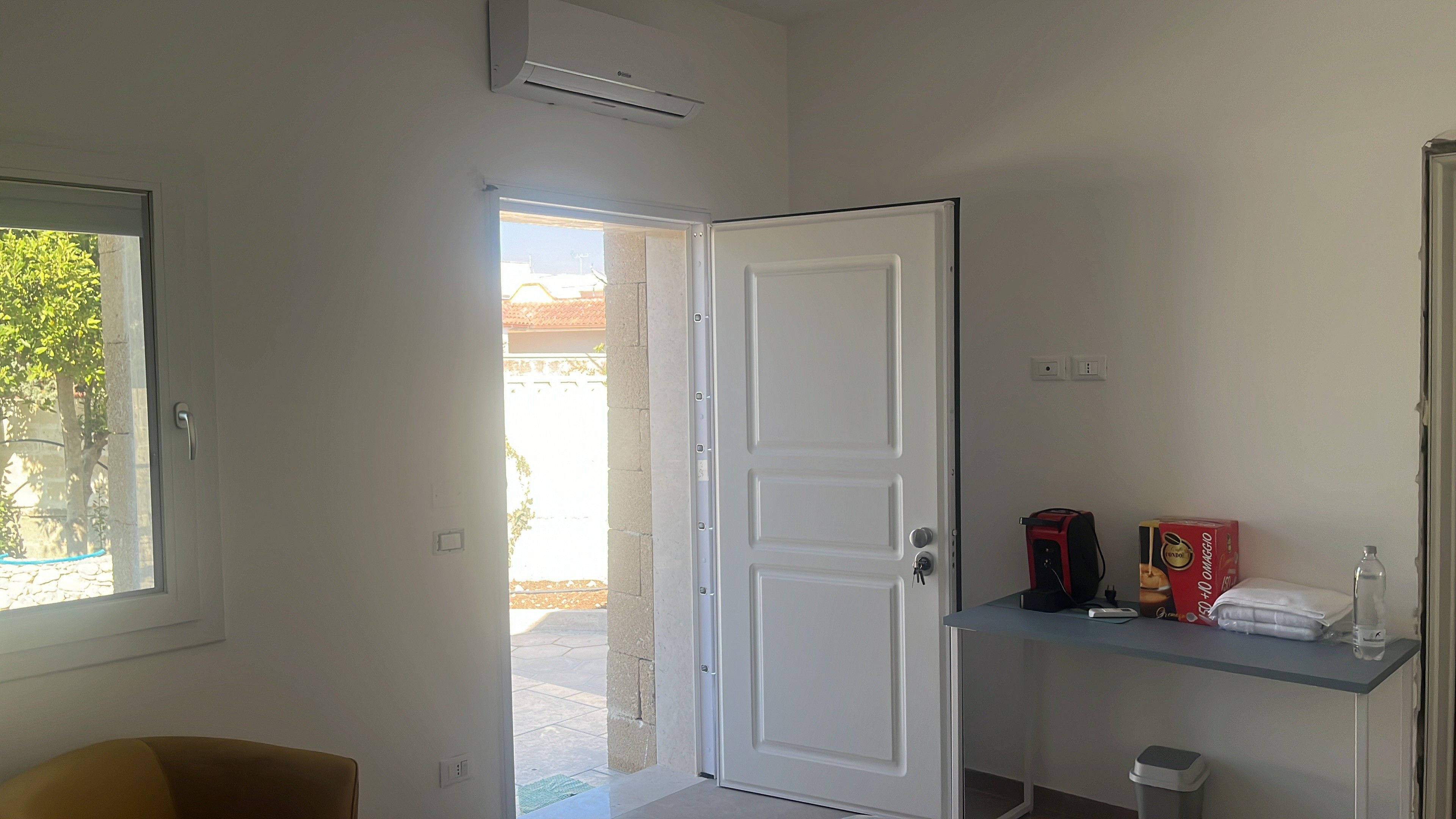 Ein Zimmer mit einer weißen Tür, einem Fenster und einem kleinen Regal mit Gegenständen.