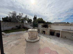 Un patio con un hogar de piedra, una parrilla empotrada y un piso de baldosas hexagonales.