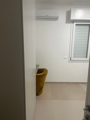 Ein Zimmer mit einer weißen Wandairconditioner, einem Fenster mit Jalousien und einem gelben Mülleimer.