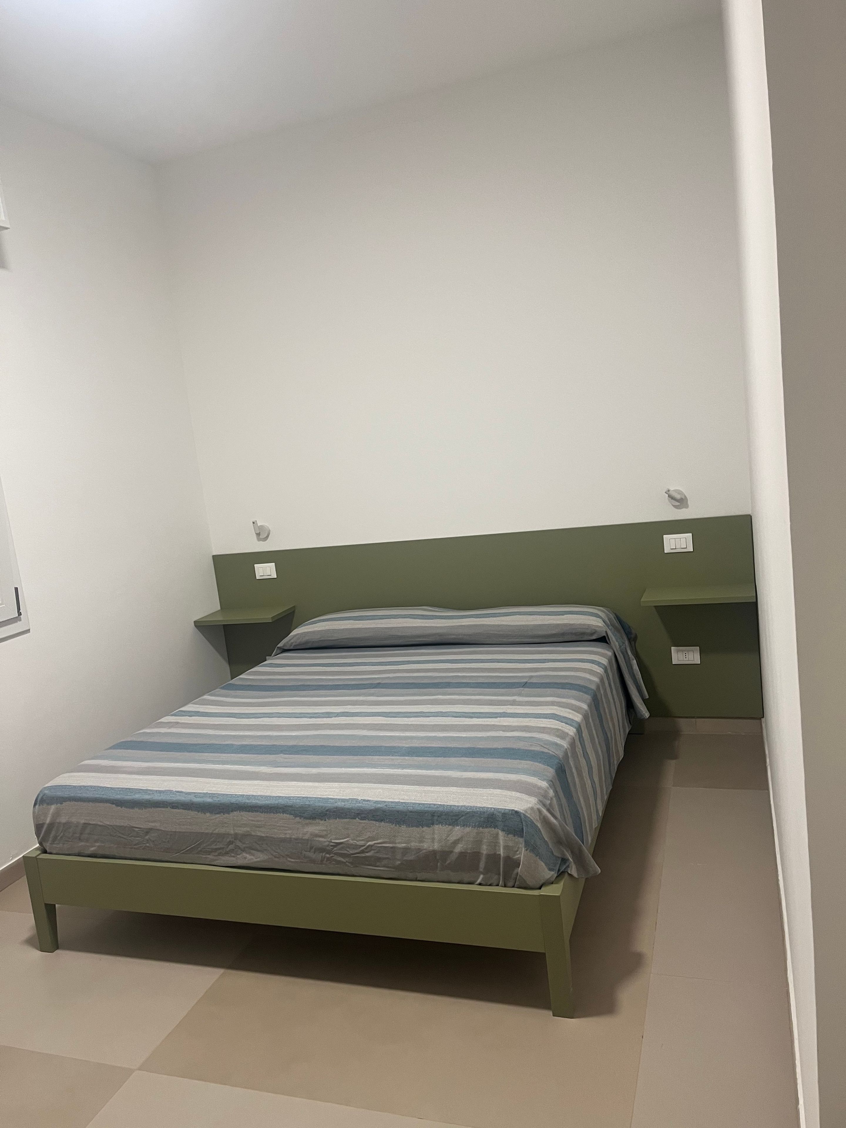 Une chambre avec un lit simple, une tête de lit verte, une table de chevet et une petite table à côté du lit.