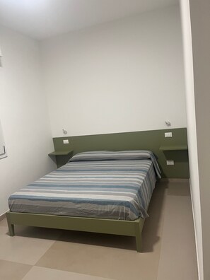 Ein Zimmer mit einem Einzelbett, einem grünen Kopfteil, einem Nachttisch und einem Beistelltisch.
