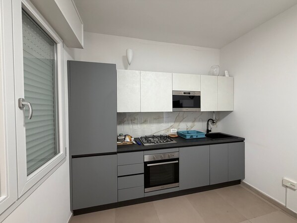 Cocina compacta con armarios grises, horno integrado, cocina a gas y encimera negra.