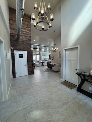 A spacious interior with a high ceiling, a central chandelier, and a modern kitchen in the background. - Deluxe Las Cruces Retreat: Mountain Views, Secure Outdoor Oasis, Modern Comforts (Las Cruces)