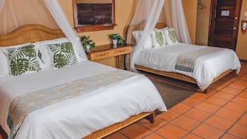 A hotel room with two beds, a wooden headboard, a bedside table with a plant, and a mirror on the wall.