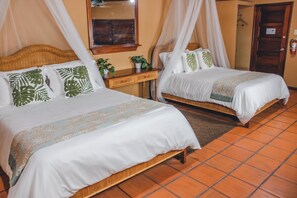 A hotel room with two beds, a wooden headboard, a bedside table with a plant, and a mirror on the wall.