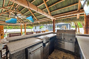 Un espacio de cocina al aire libre con una parrilla, una mesa de comedor y una zona de estar con sillas.