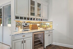 Una cocina con armarios blancos, cafetera espresso integrada, refrigerador para vinos y un salpicadero con diseño.