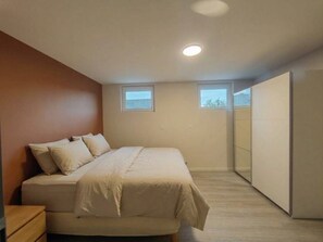 Une chambre à coucher avec un lit, une table de chevet, deux fenêtres et une armoire.