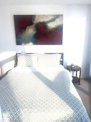 Un dormitorio con cama, mesita de noche y un cuadro abstracto colgado en la pared.