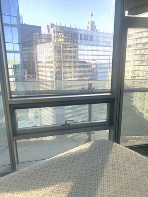 Vista a través de una ventana con un cojín estampado, baranda metálica y un paisaje urbano que incluye edificios y un río.