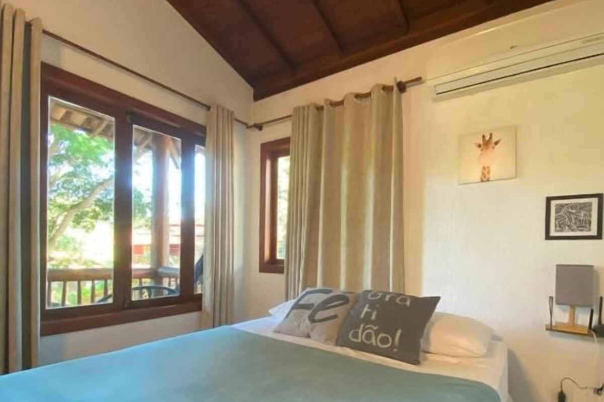 A bedroom with a bed, curtains, a wall-mounted lamp, and a window with a view.