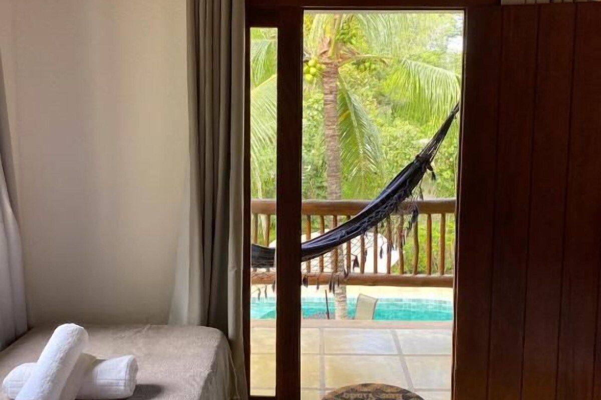 A room with a bed, a view of a pool, and a hammock outside.