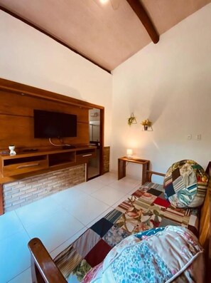 A room with a television mounted on a wooden wall, a small table with a candle, and a patterned rug on the floor. - Maui Suítes e Chalés (Arraial d'Ajuda)
