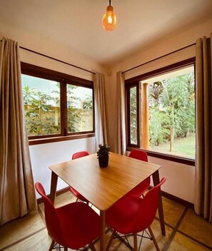 A room with a wooden table and red chairs, large windows with curtains, and a hanging light fixture. - Maui Suítes e Chalés (Arraial d'Ajuda)