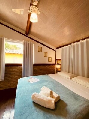 A hotel room with a bed, a ceiling fan, a window with curtains, and a brick wall. - Maui Suítes e Chalés (Arraial d'Ajuda)