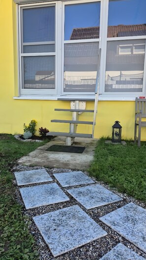 A yellow building with a window, a metal bench, a lantern, and a paved pathway. - Guest House 'Monday's Ferienwohnung' with Wi-Fi (Wehr)