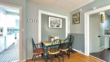 A dining area with a wooden table and chairs, a picture on the wall, and a view of the outside.