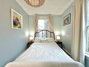 A bedroom with a bed, two bedside tables with lamps, a window with curtains, and two framed pictures on the walls. - Dream Suite near LaHave River in DT Bridgewater (Bridgewater)